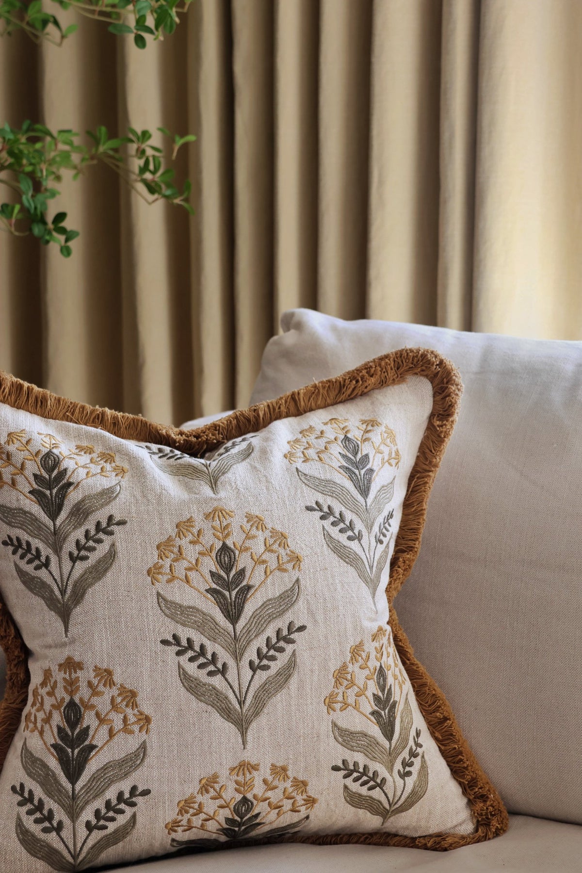 embroidery pattern cushion with floral pattern on a couch against a curtain background