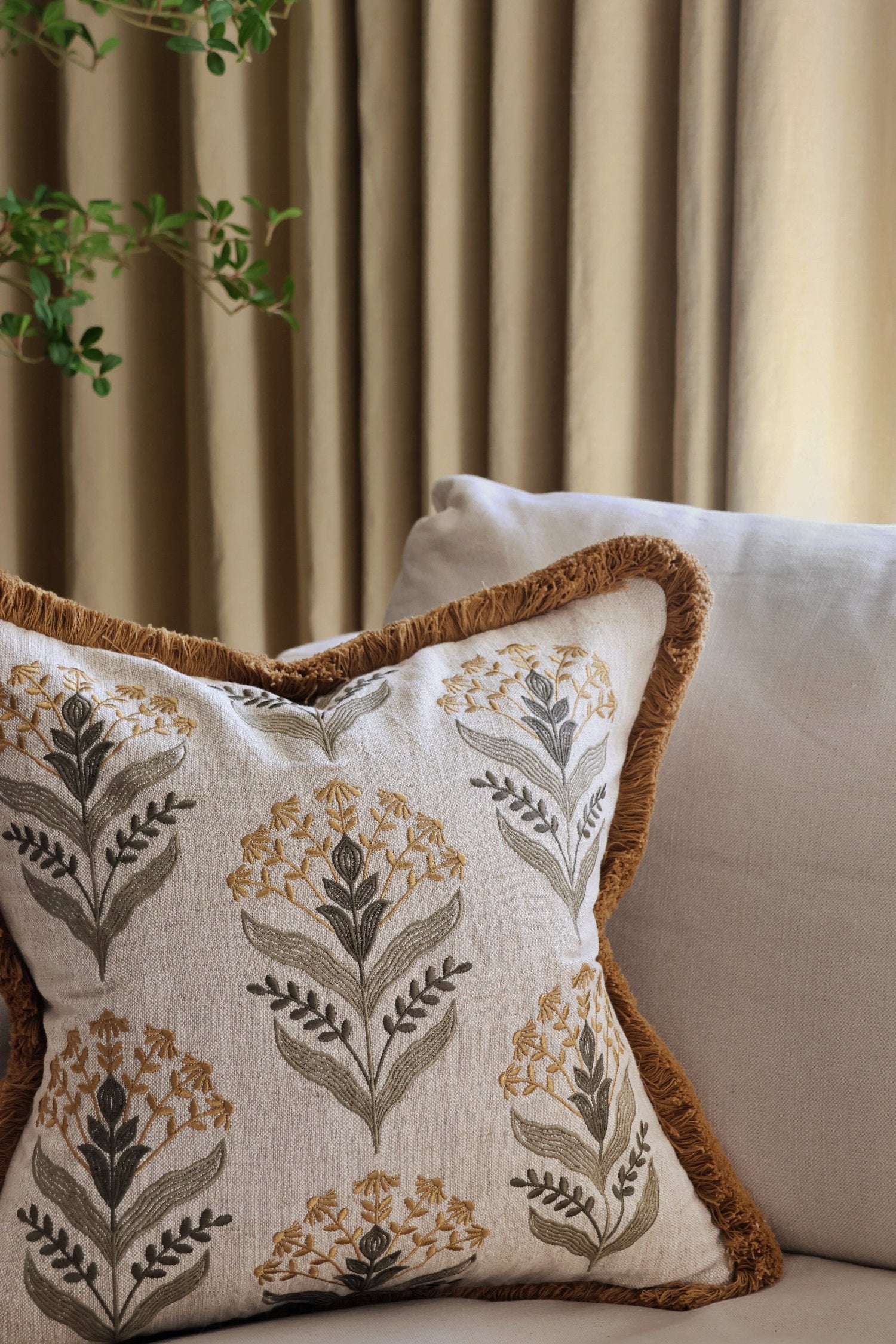 embroidery pattern cushion with floral pattern on a couch against a curtain background