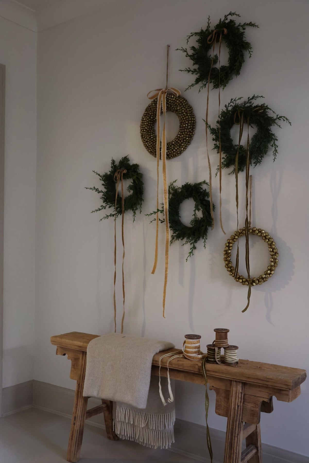 decorating artificial wreaths and bell wreaths hanging on a wall with long trailing ribbons with a vintage wooden bench underneath