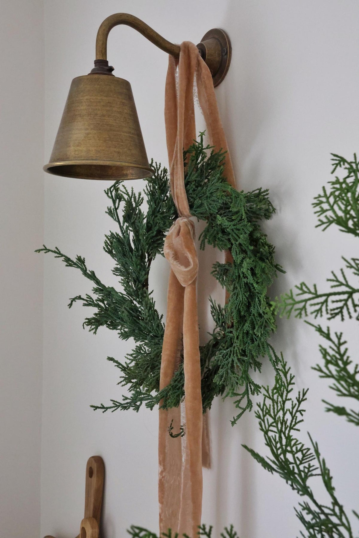 Decorative wall sconce with a green wreath and pink ribbon against a white wall.