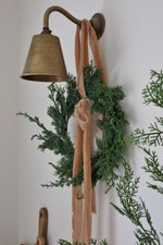 Decorative wall sconce with a green wreath and pink ribbon against a white wall.
