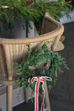 mini faux cypress wreath on back of rattan chair and hanging red ribbon