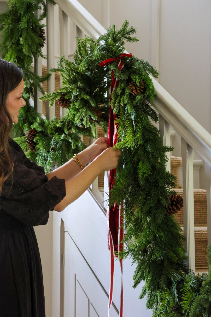 A woman touching an artificial christmas garland on a staircase