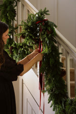 women arranging faux green xmas garland on stairs with red ribbon