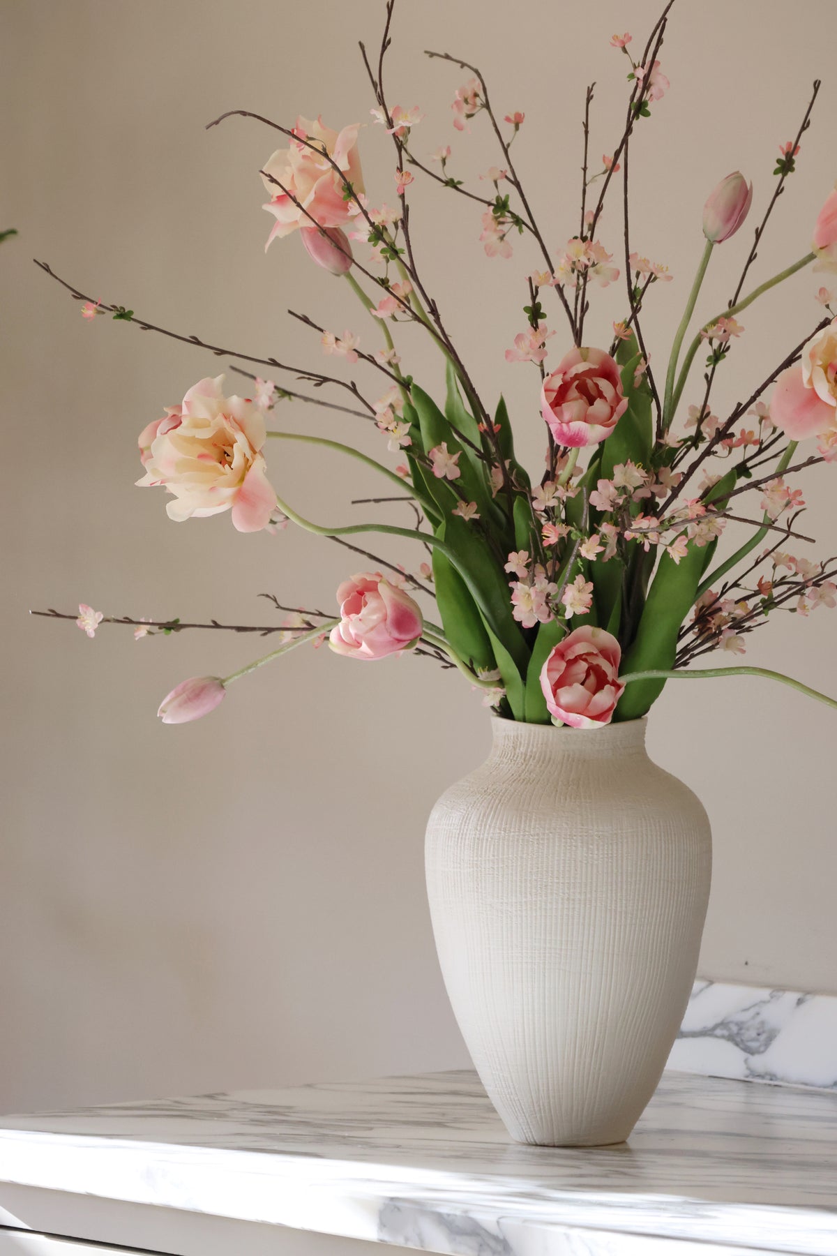 White vase with pink and green flowers on a marble surface