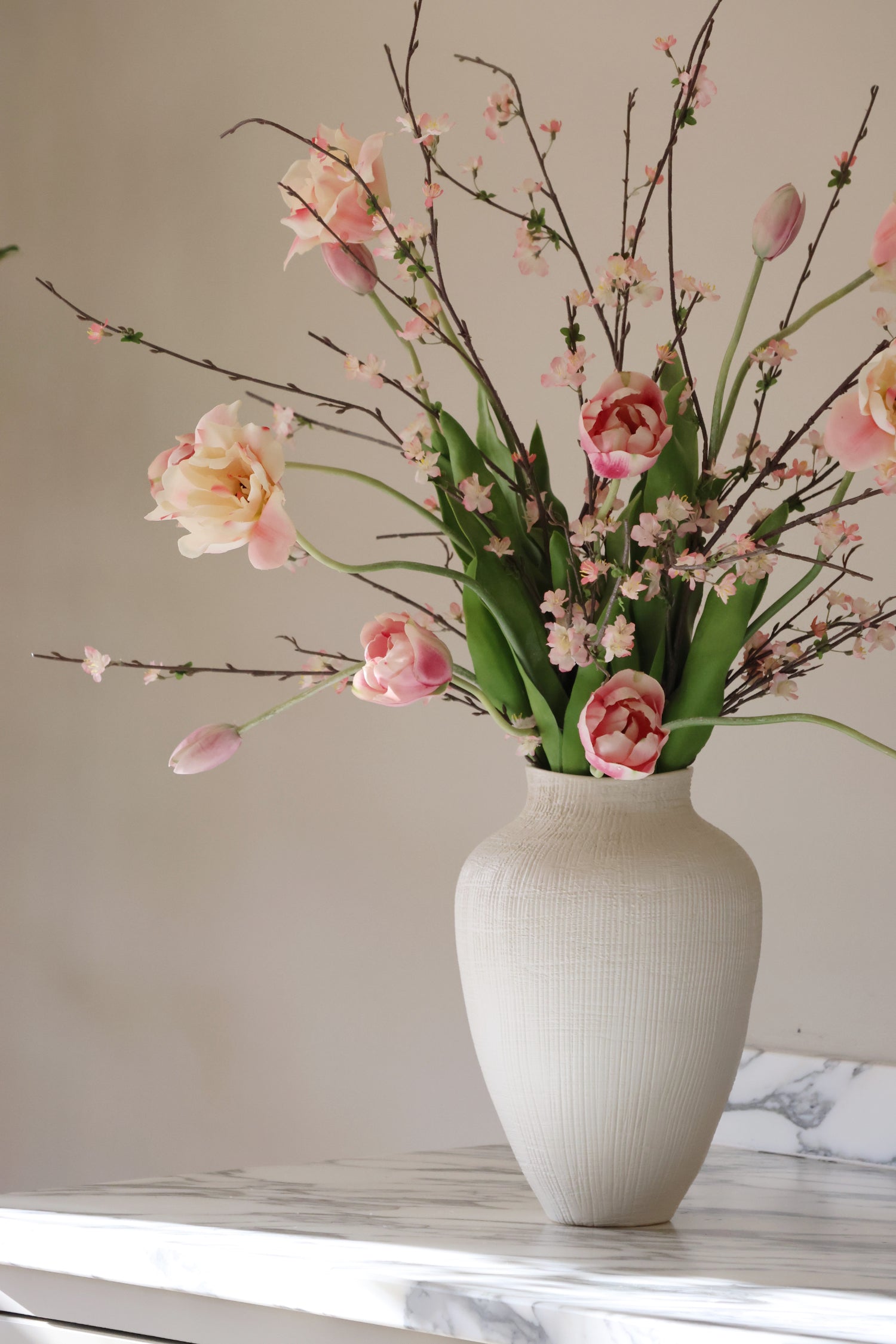 White vase with pink and green flowers on a marble surface