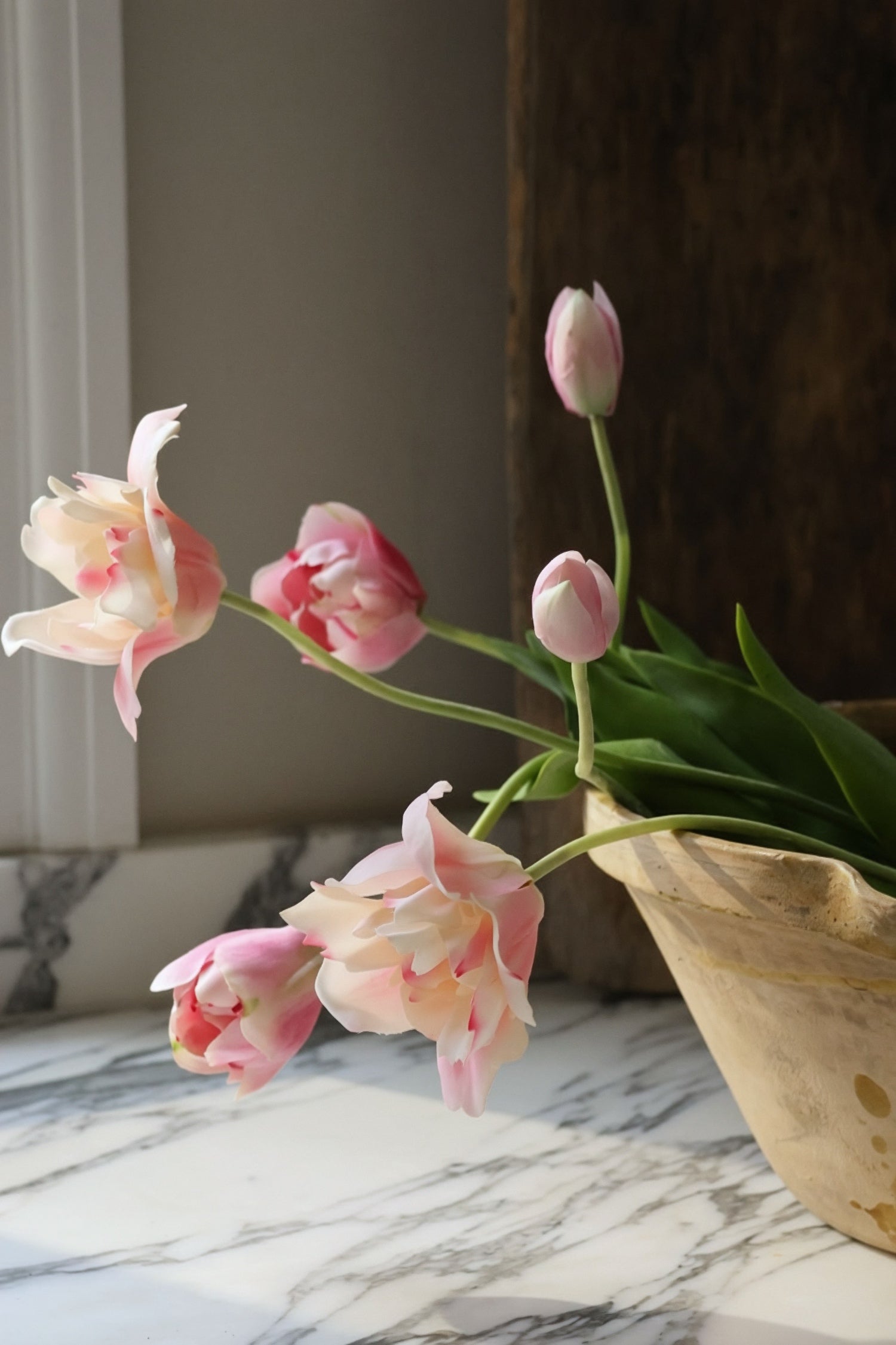 Pink tulips in a ceramic pot on a marble surface with a neutral background