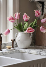 Pink tulips in a white vase on a marble countertop with a window in the background.