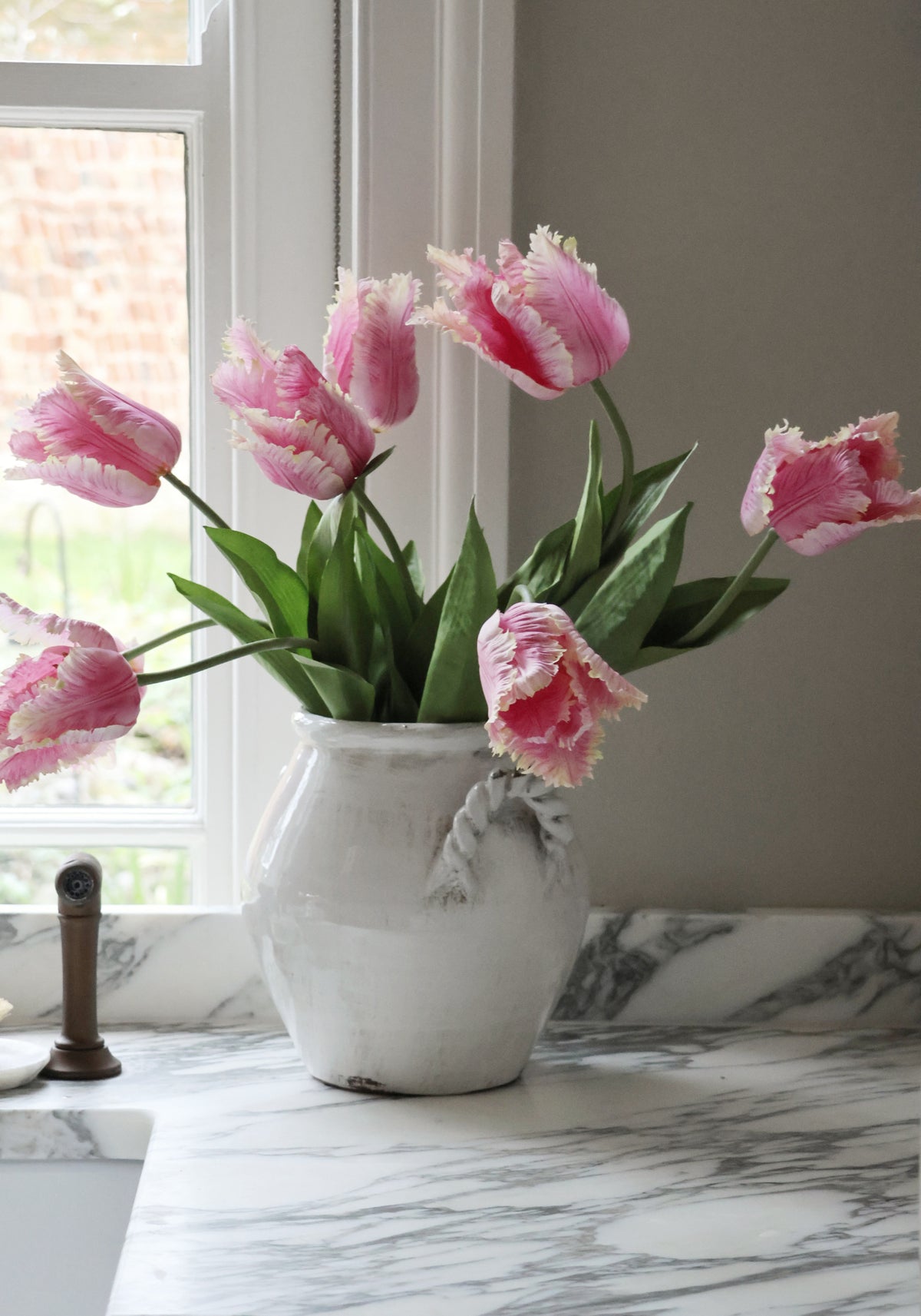 Pink tulips in a white vase on a marble surface with a window in the background