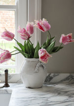 Pink tulips in a white vase on a marble surface with a window in the background