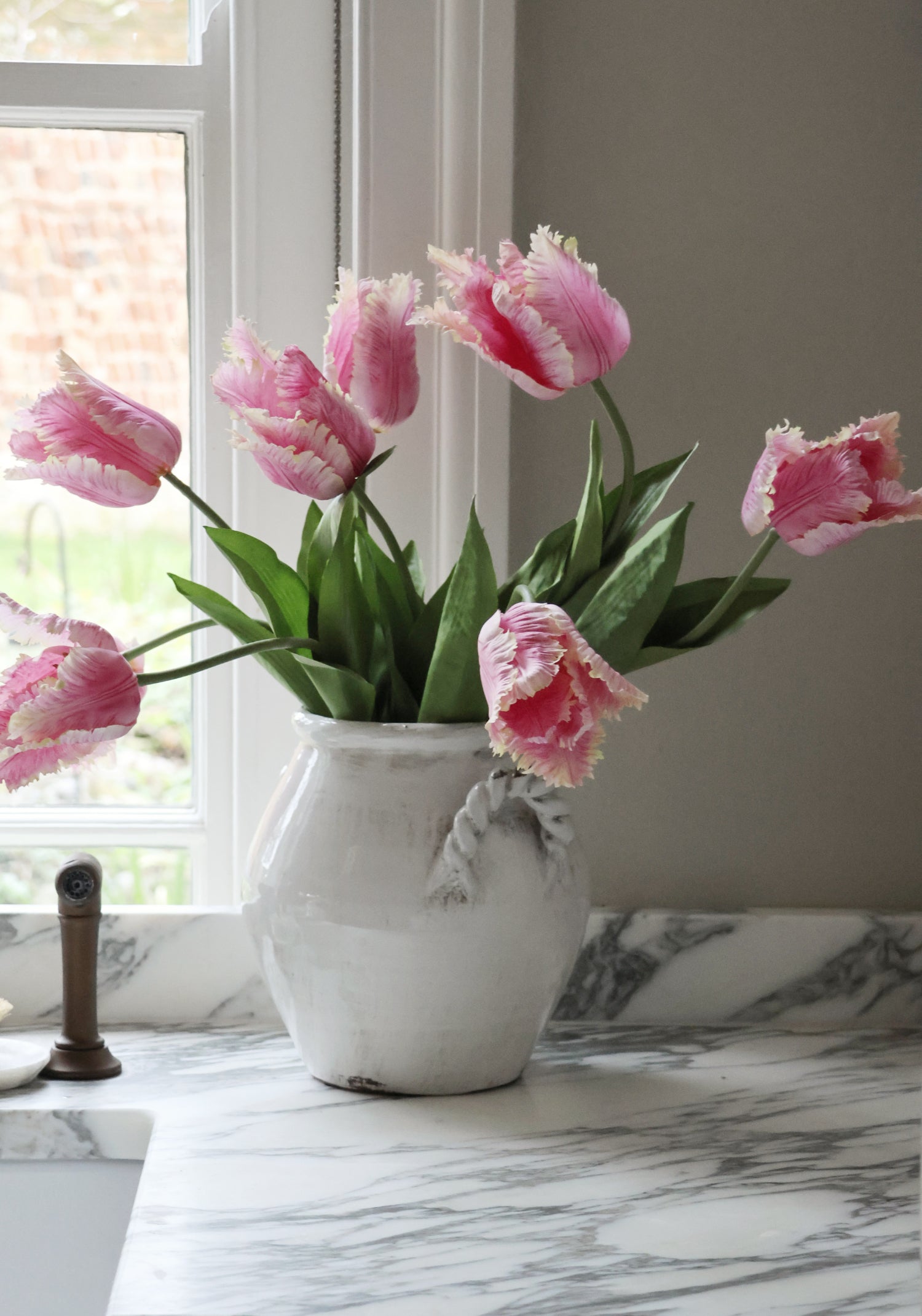 Pink tulips in a white vase on a marble surface with a window in the background