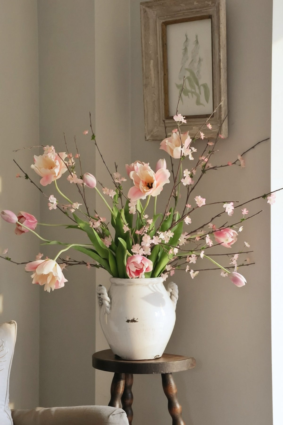Floral arrangement in a white vase on a wooden side table against a gray wall with a framed picture.