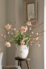 Floral arrangement in a white vase on a wooden side table against a gray wall with a framed picture.