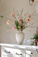 White vase with pink flowers on a white surface