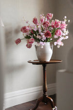 White vase with pink and white flowers on a wooden side table against a neutral wall.