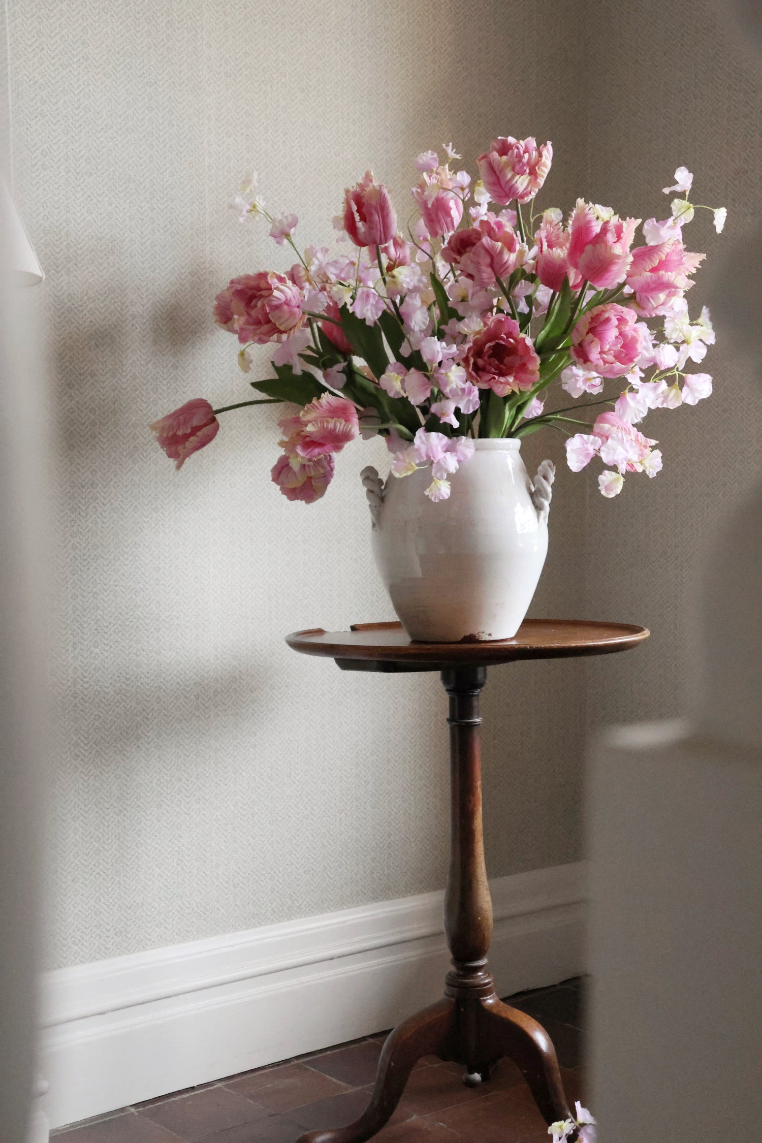 White vase with pink and white flowers on a wooden side table against a neutral wall.