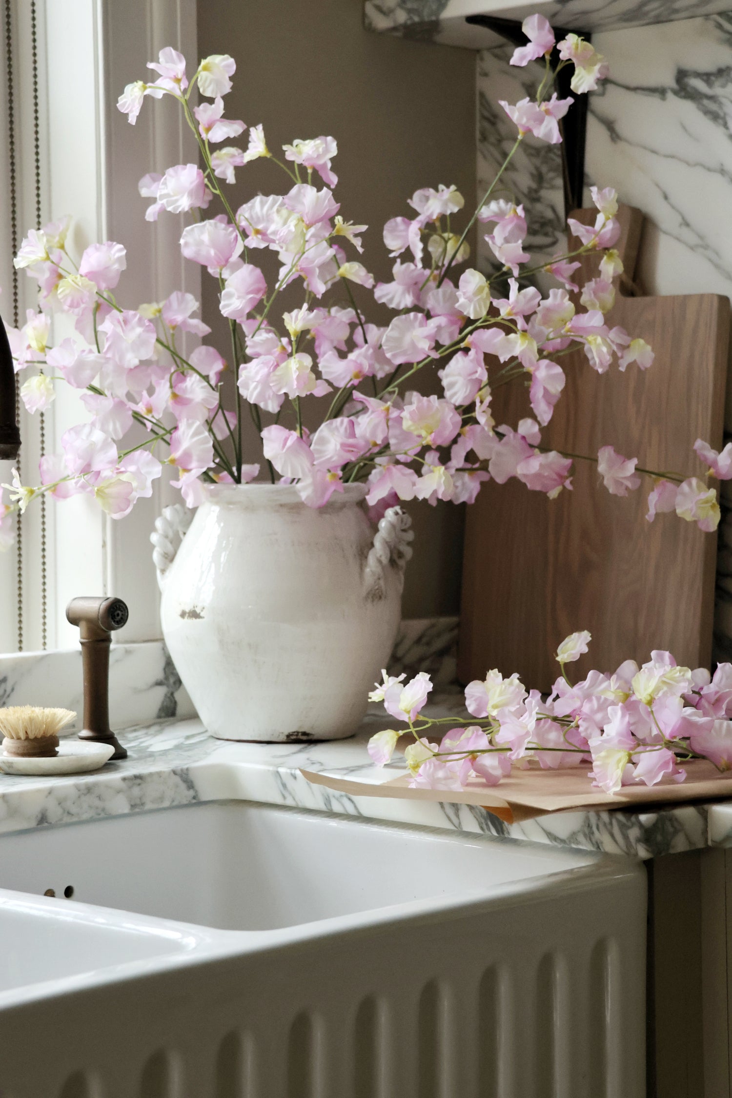Pink flowers in a white vase on a kitchen counter with marble backsplash