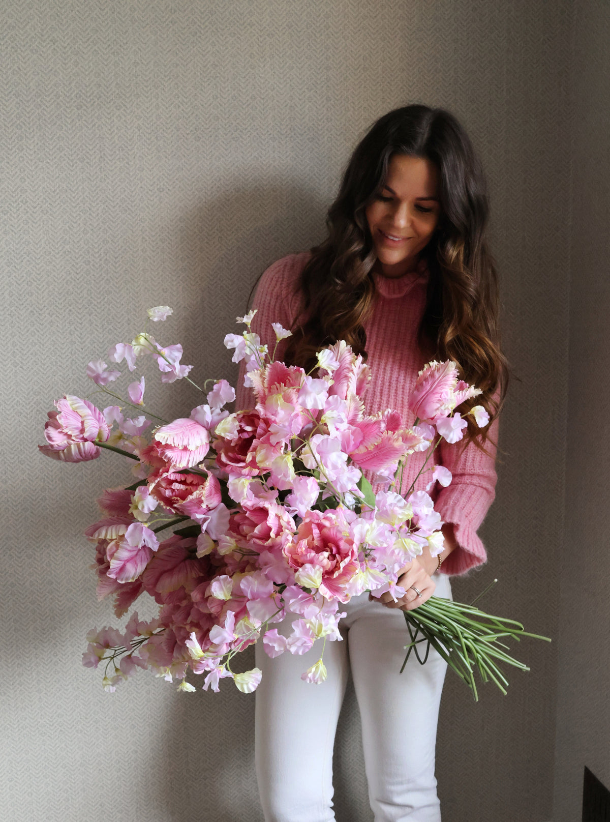 Woman holding a bouquet of pink flowers against a plain background