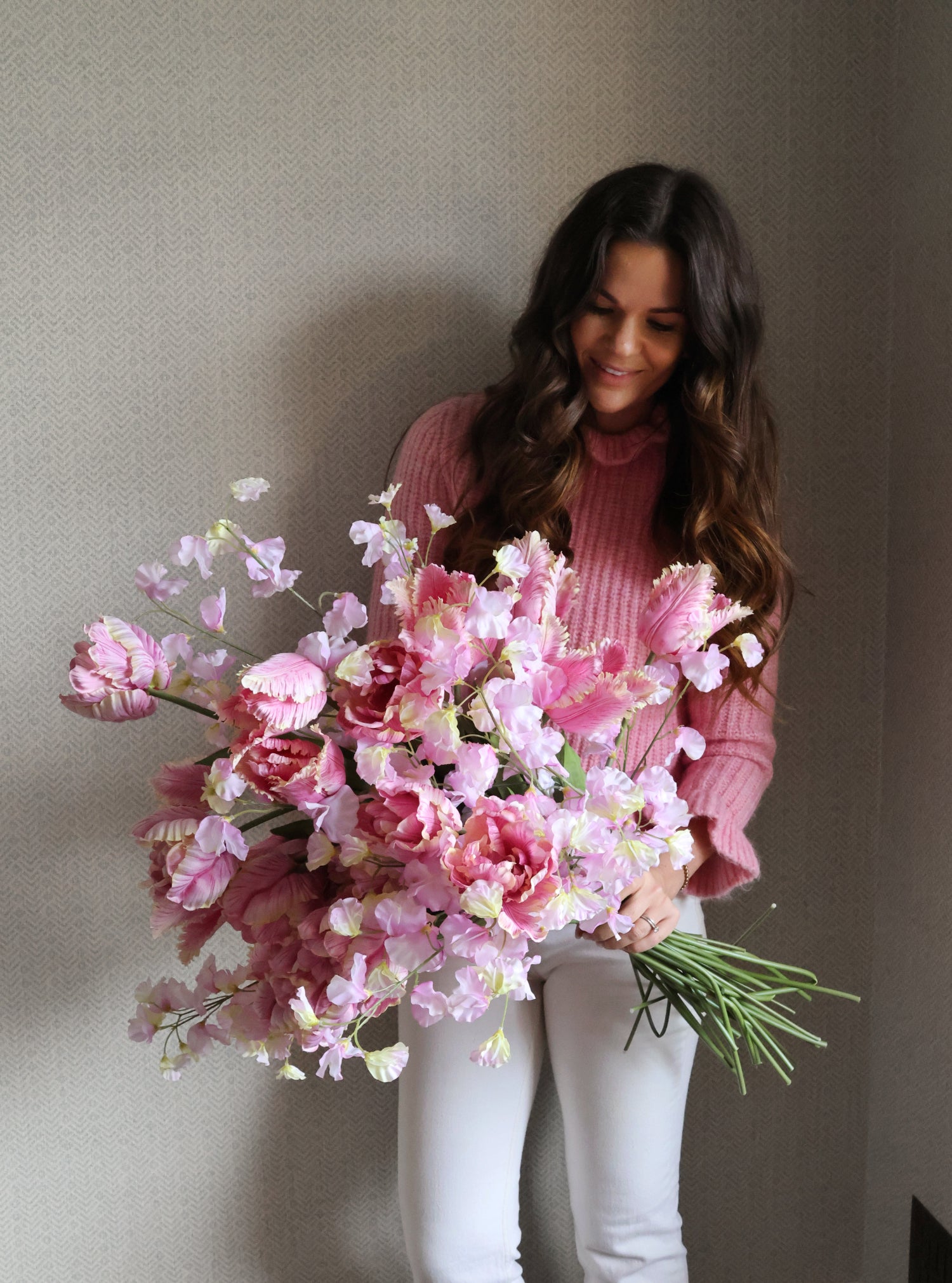 Woman holding a bouquet of pink flowers against a plain background