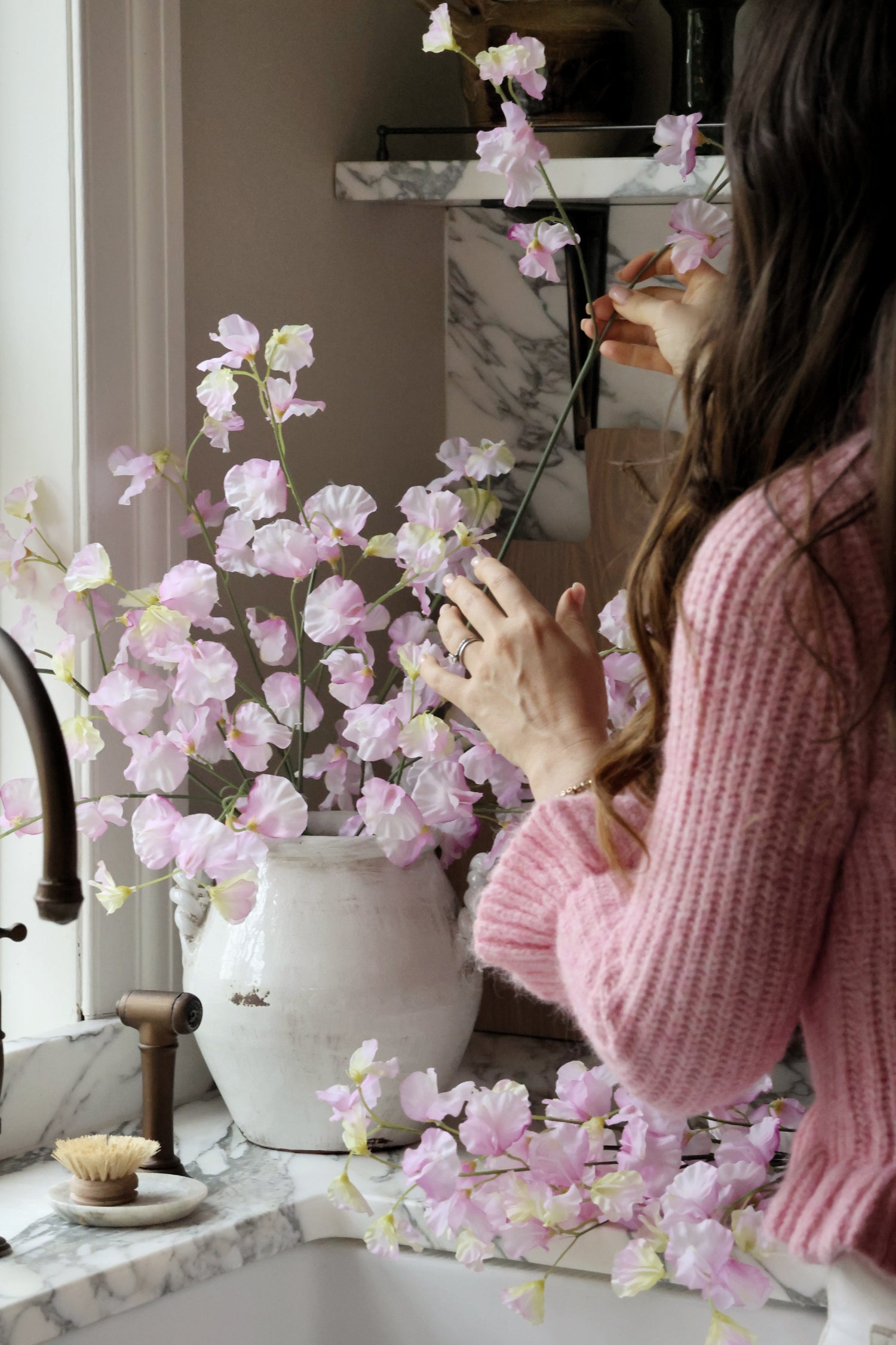 Person arranging pink flowers in a vase on a kitchen counter