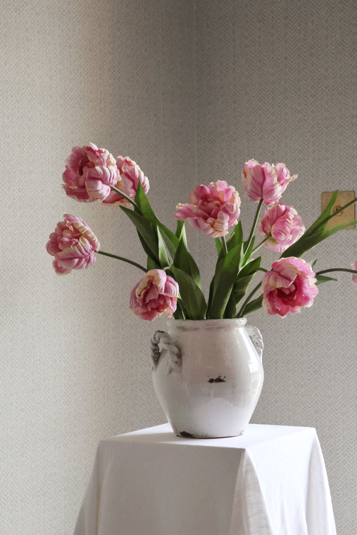 white vase with pink tulips in on textured background 