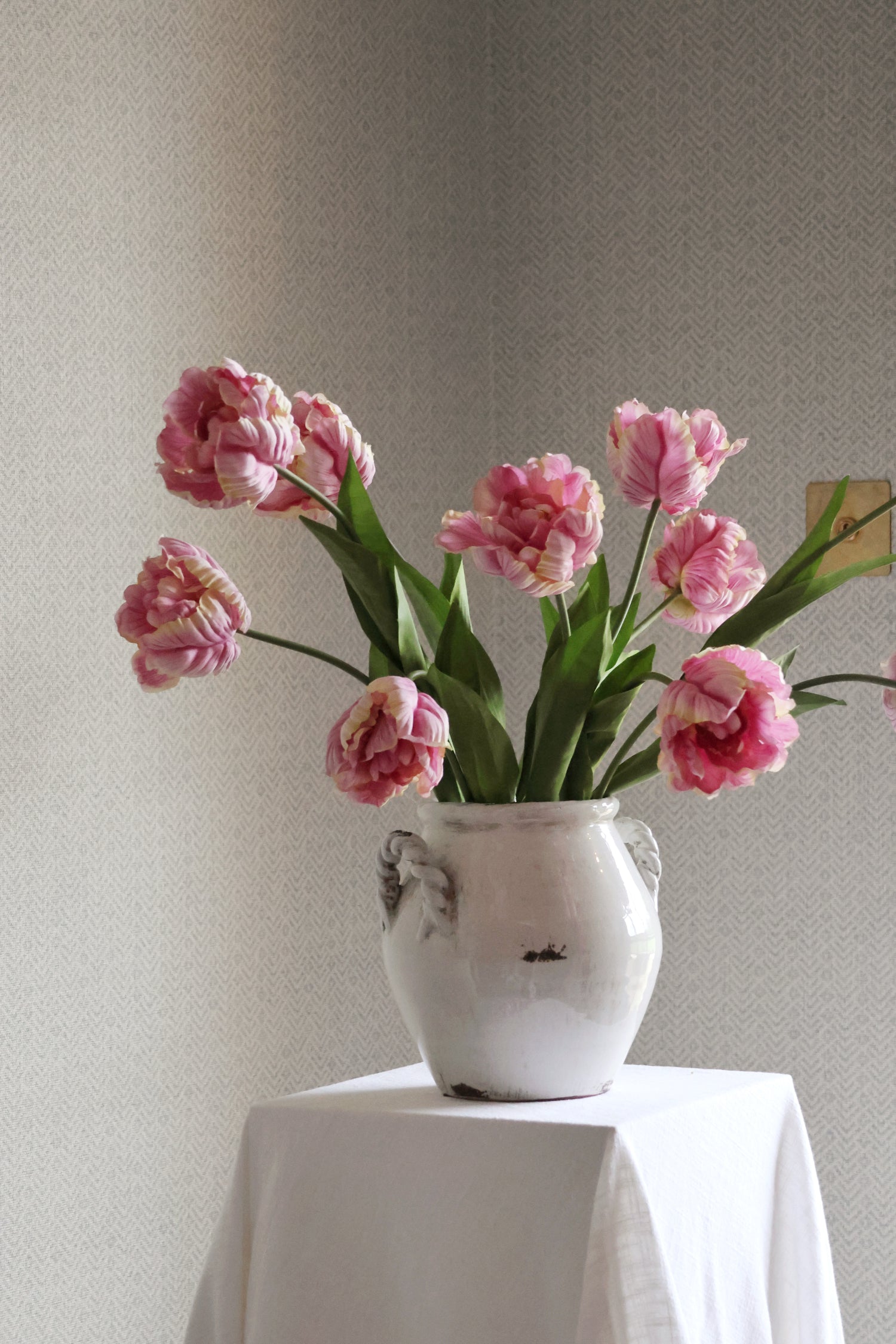 white vase with pink tulips in on textured background 