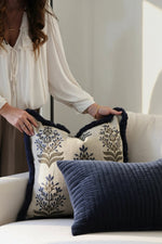 person arranging blue cushions on a beige sofa 