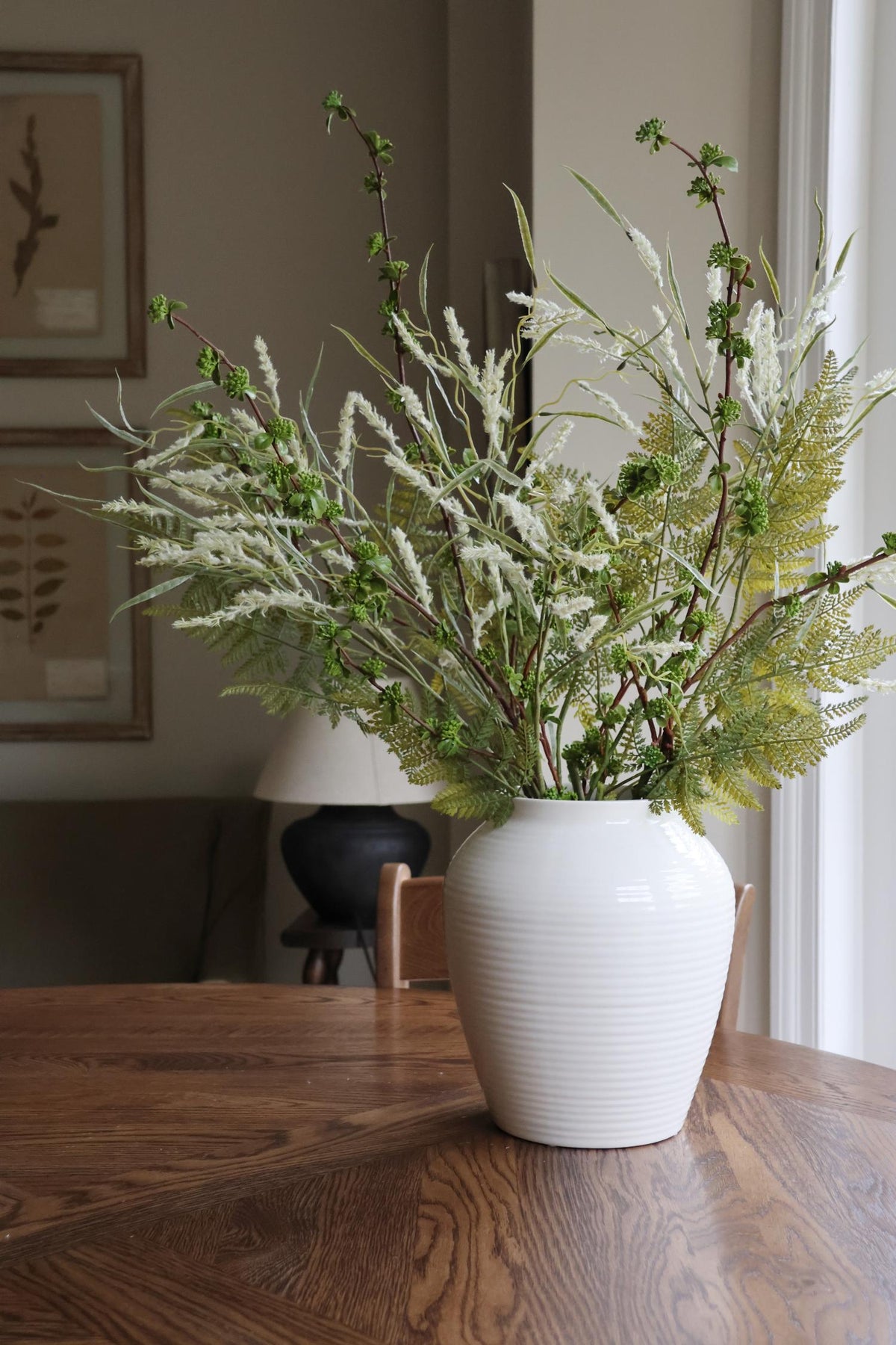 faux summer foliage arrangement in white ceramic vase on wooden table 