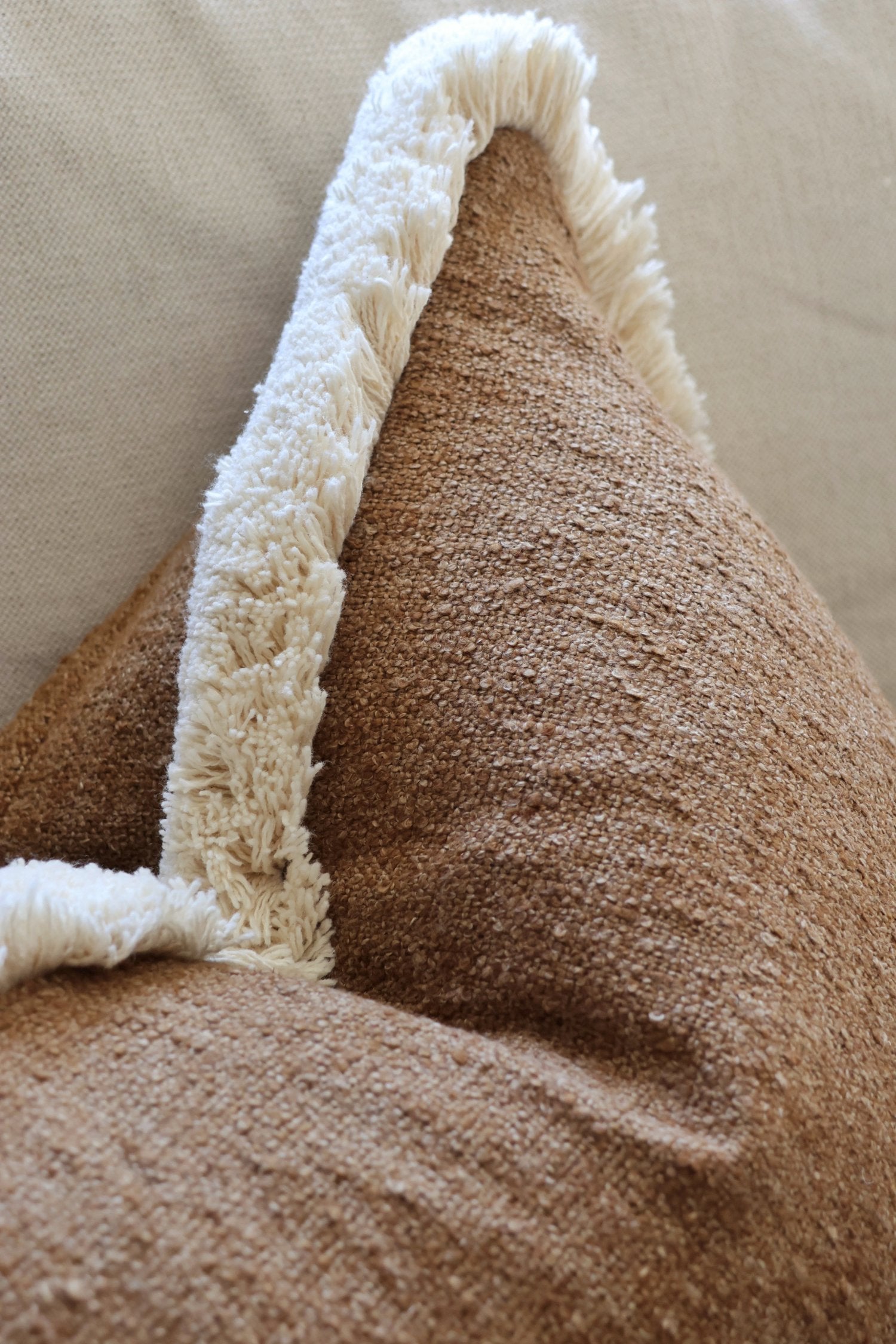 Brown textured cushion with white fringe trim on a beige background