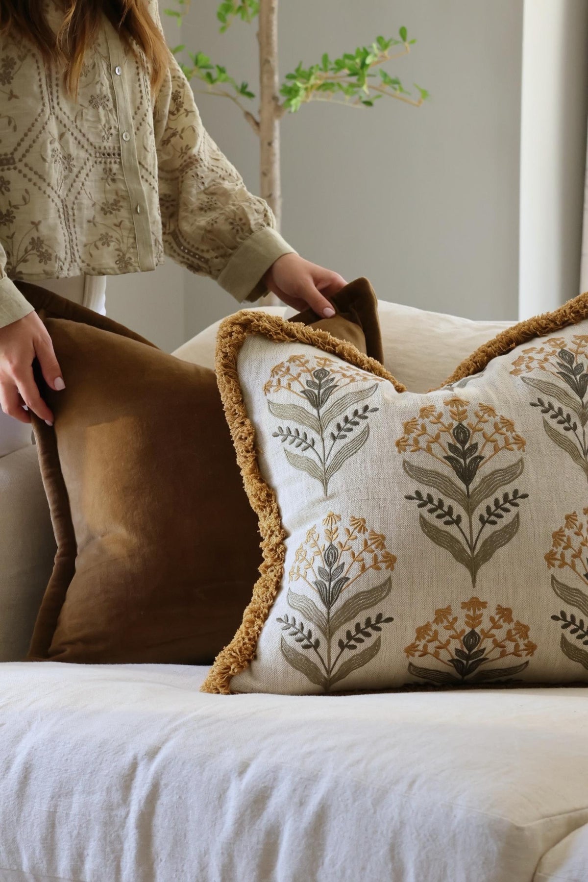Person arranging decorative cushions on a sofa with a neutral background