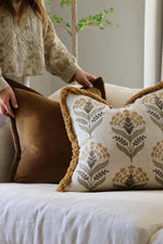 Person arranging decorative cushions on a sofa with a neutral background