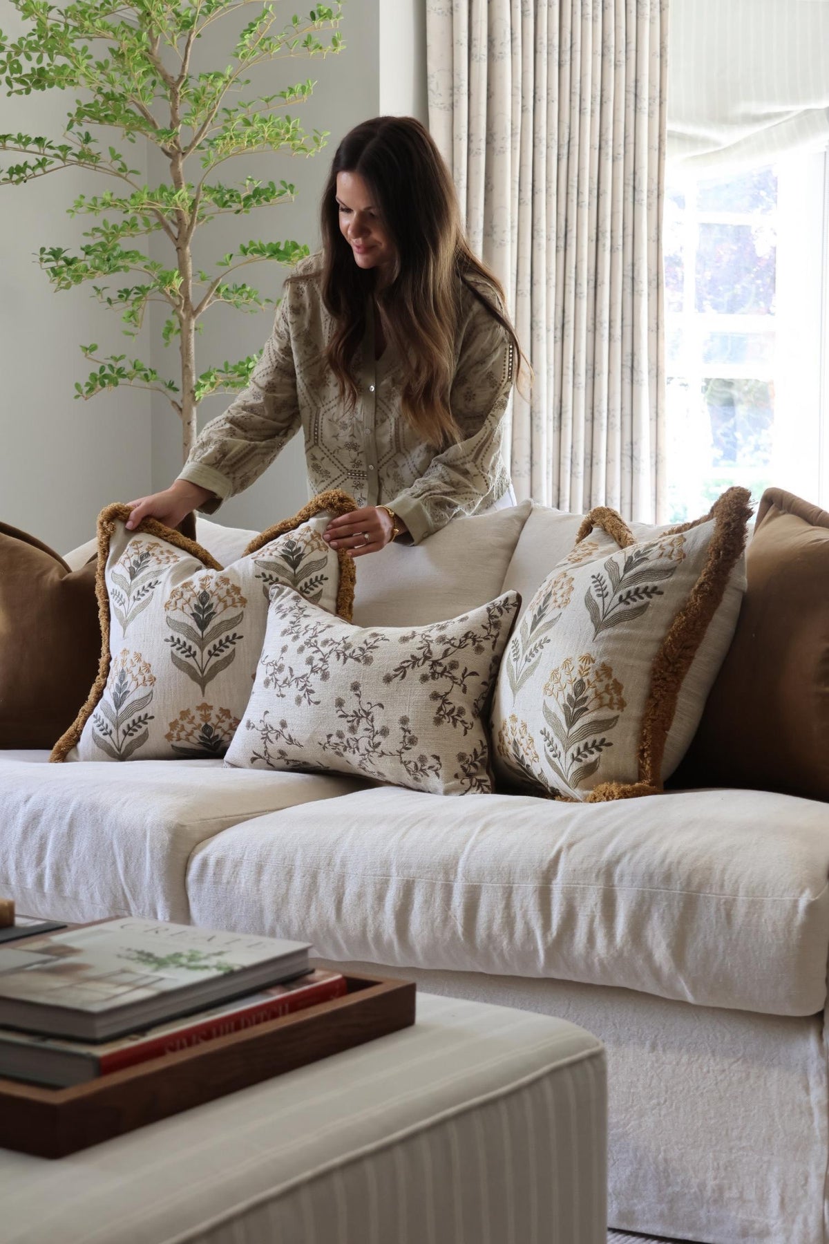Woman arranging decorative cushions on a white sofa in a stylish living room.