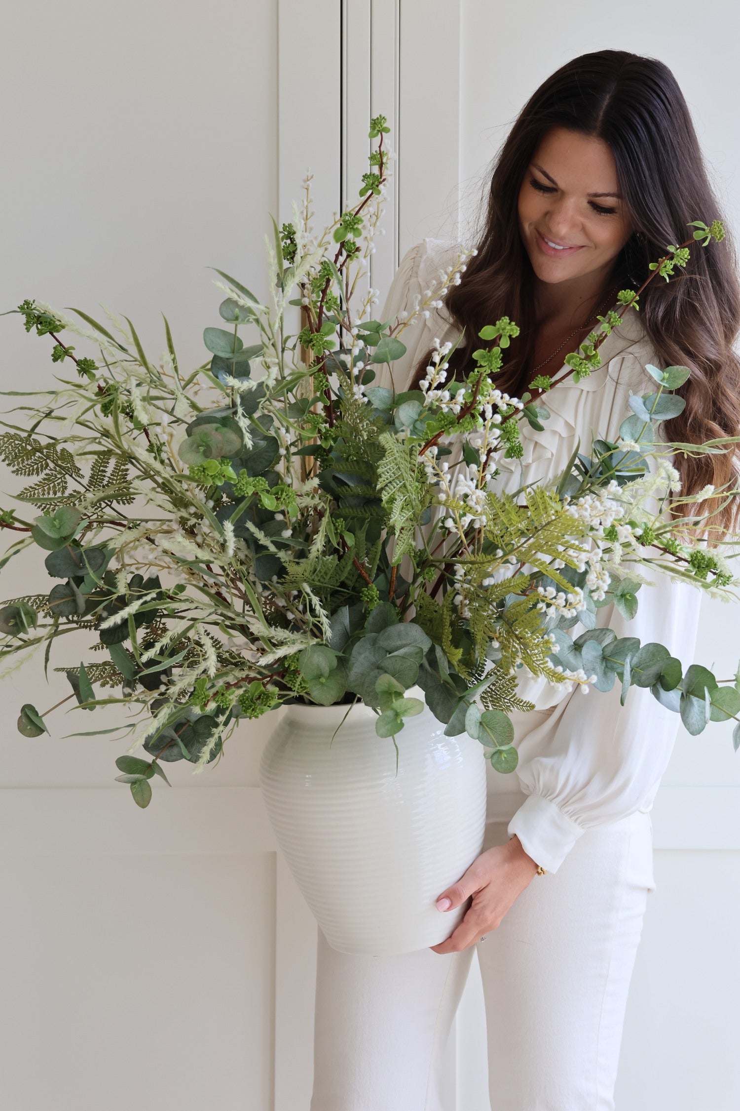 Woman holding a large bouquet of greenery against a white background