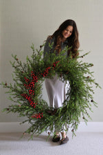 Woman holding a large artificial wreath with red berries against a plain background