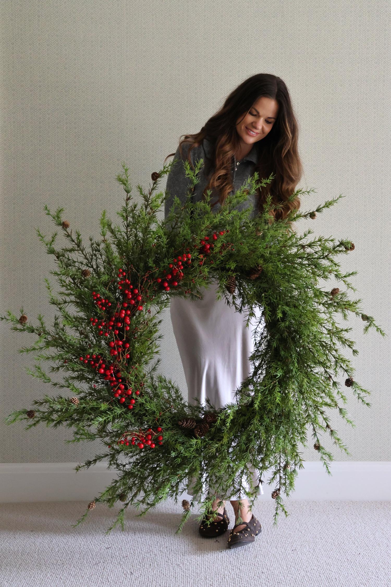 Woman holding a large artificial wreath with red berries against a plain background