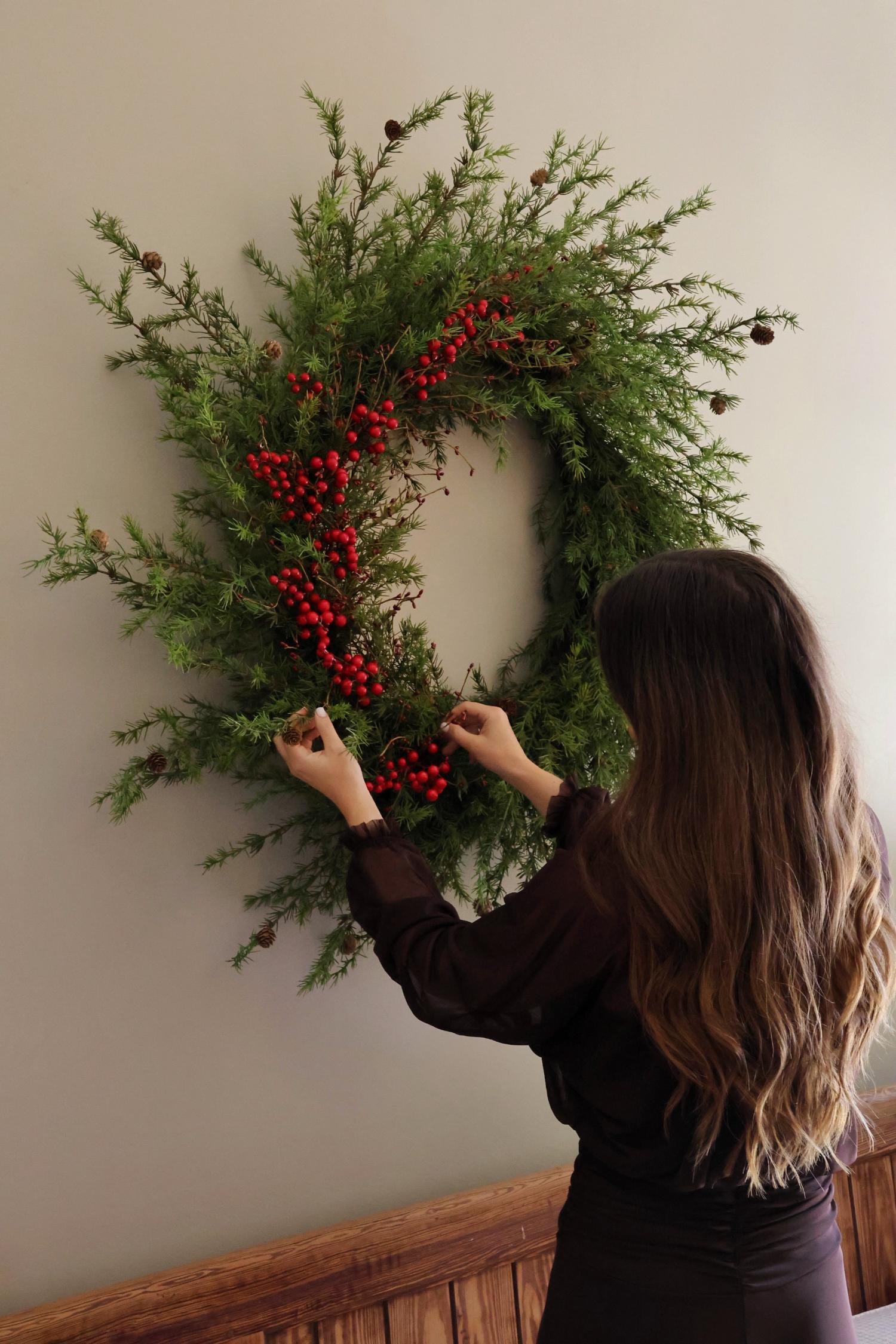 Person adjusting an artificial festive wreath with red berries on a wall.