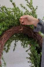 Hand adjusting a rattan wreath base on a plain background