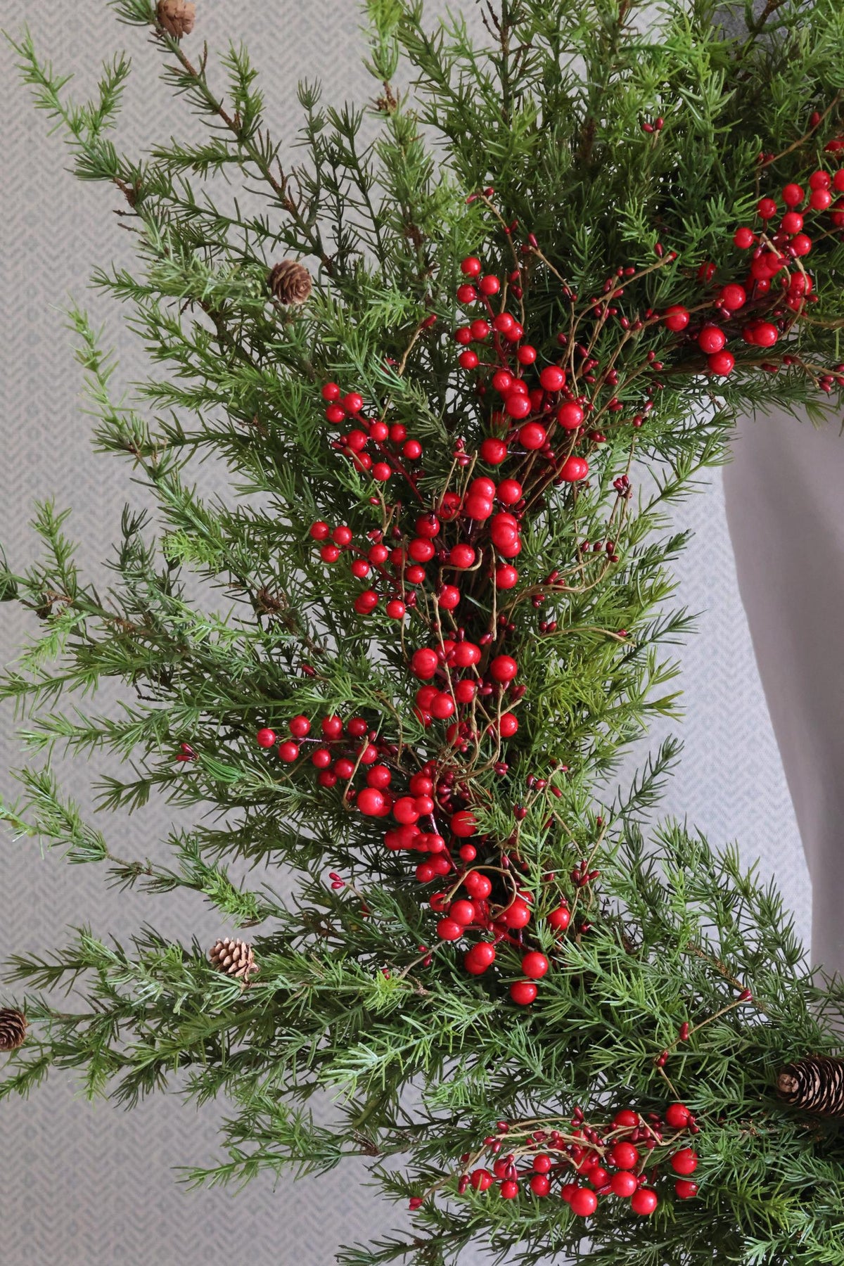 Decorative artificial christmas wreath with green foliage and red berries on a neutral background
