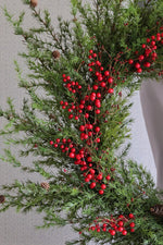 Decorative artificial christmas wreath with green foliage and red berries on a neutral background