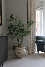 artificial luxury olive tree with large trunk in a beige stone effect planter in a living room setting 