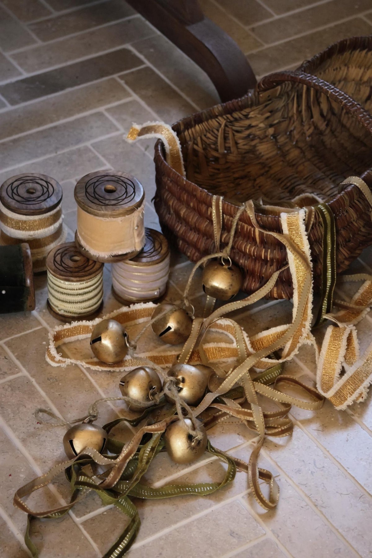 a collection of brass bells and gold and taupe velvet ribbons on a tiled herringbone floor with vintage weave basket 