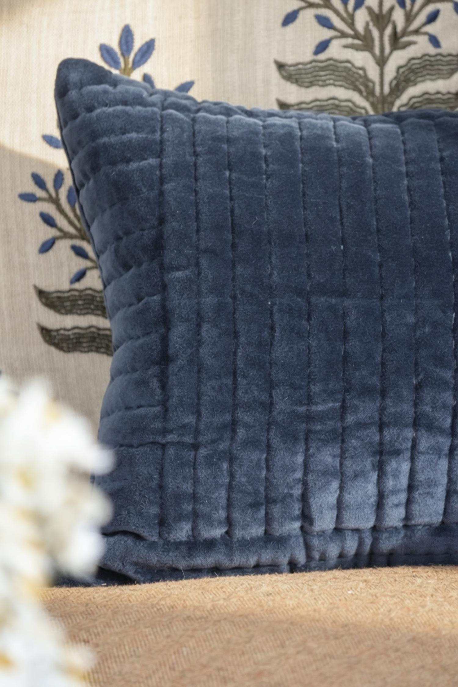 Blue textured cushion on a beige couch with a floral patterned wall in the background
