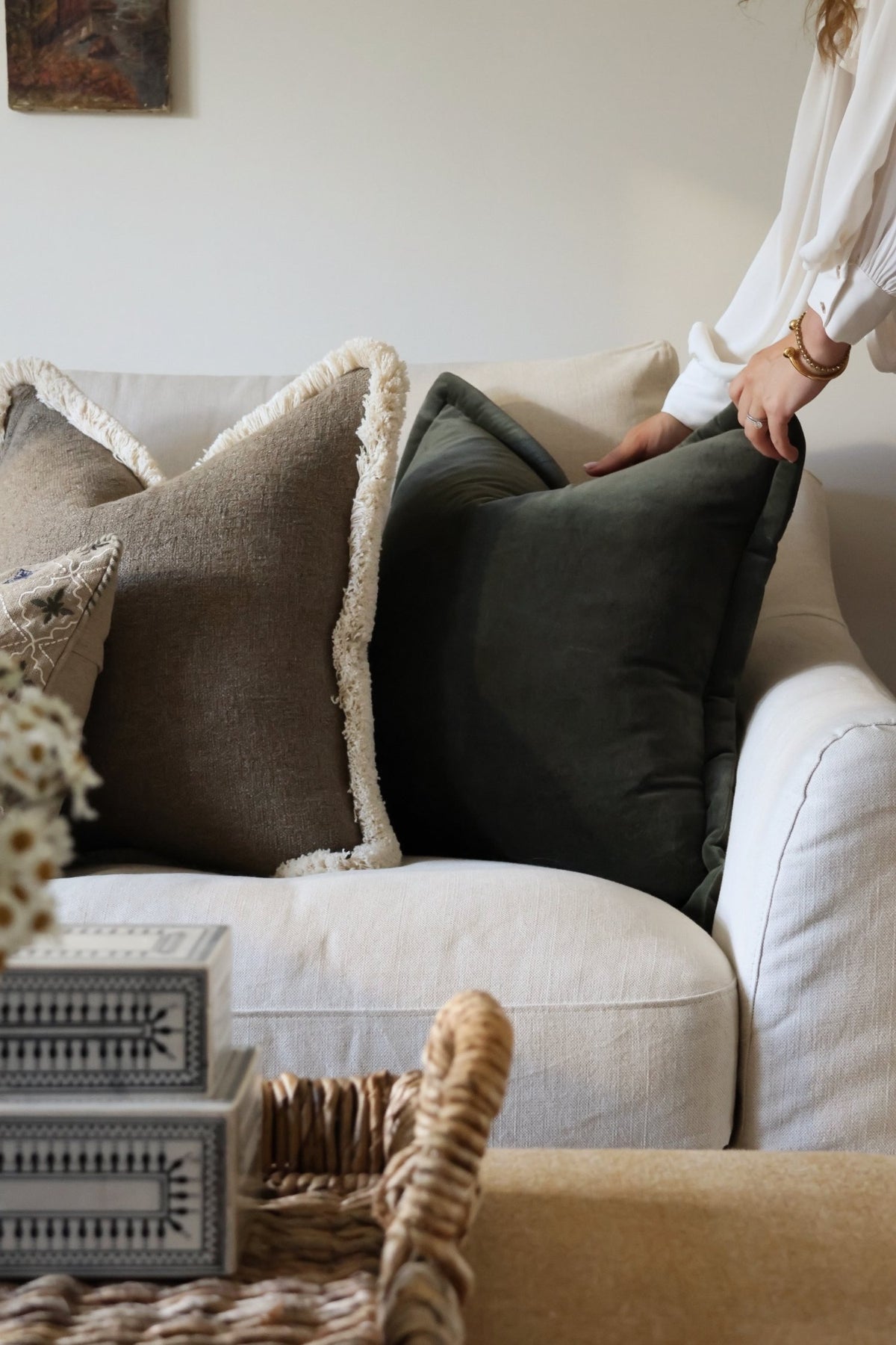 Person arranging dark green cushions on a sofa in a cozy living room.