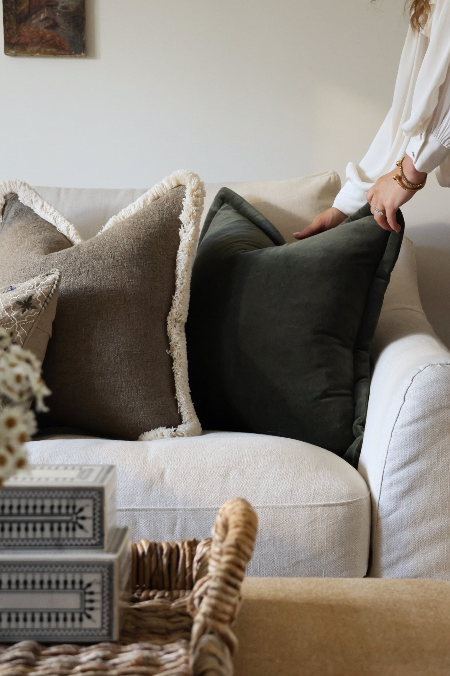 Person arranging dark green cushions on a sofa in a cozy living room.