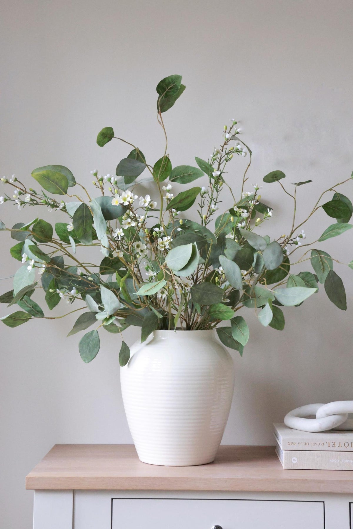 foliage and waxflower in a white vase on wooden console table neutral background 