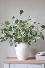 foliage and waxflower in a white vase on wooden console table neutral background 