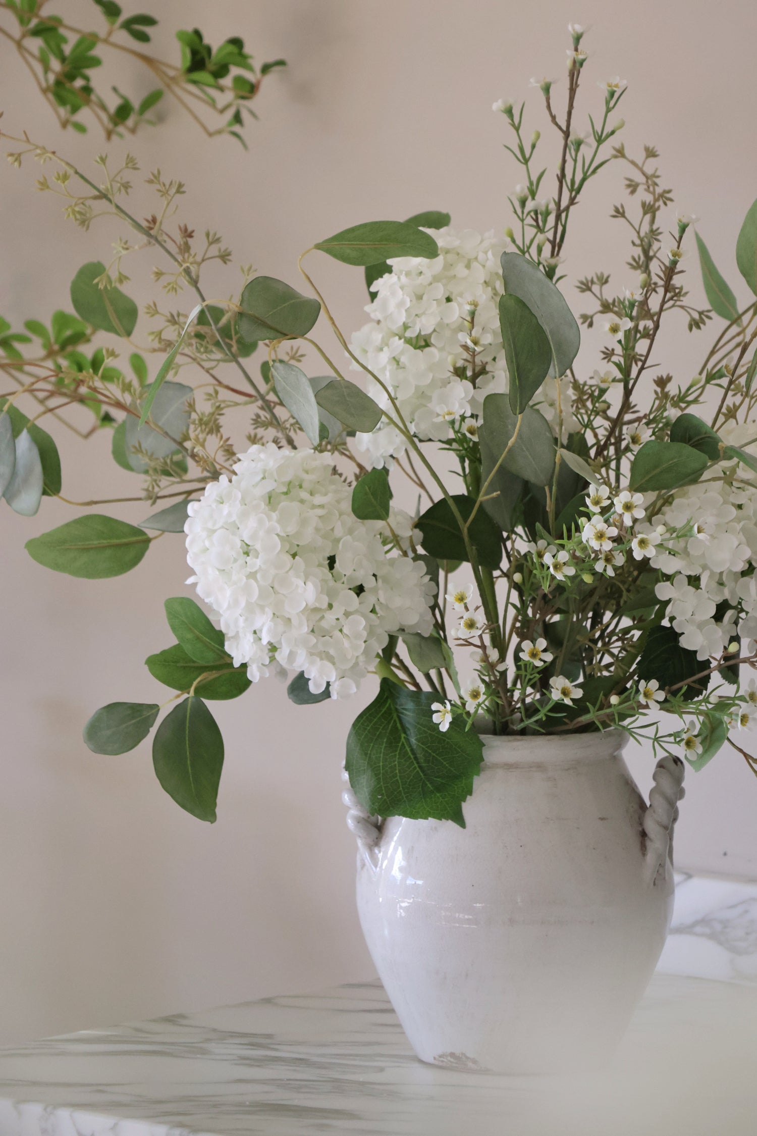 White vase with white flowers and green leaves on a neutral background