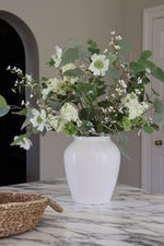 White vase with green and white flowers on a marble surface