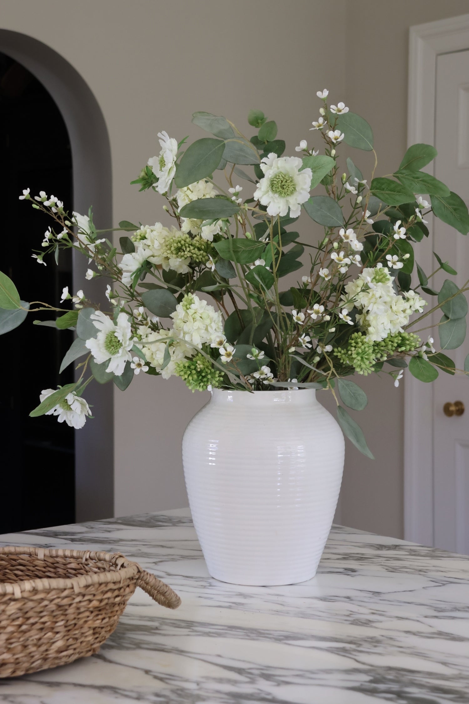 White vase with green and white flowers on a marble surface