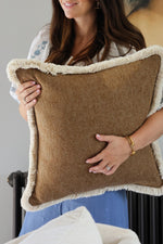 women holding textured brown cushion with beige fringe trim